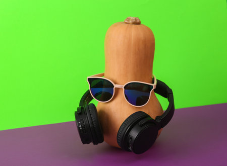 Halloween party. Halloween pumpkin with stereo headphones and sunglasses on green-purple background. creative layoutの写真素材