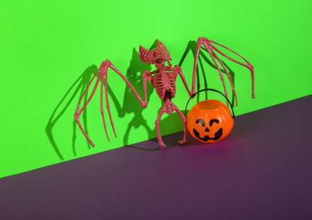 Jack o lantern halloween bucket and vampire bat on green purple background. creative halloween still lifeの写真素材