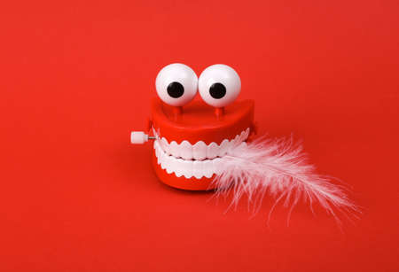 Funny toy clockwork jumping teeth with eyes holding feather on red background.の写真素材