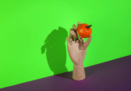 Wooden hand holds Halloween pumpkin on a green-purple background. Minimal halloween still lifeの写真素材