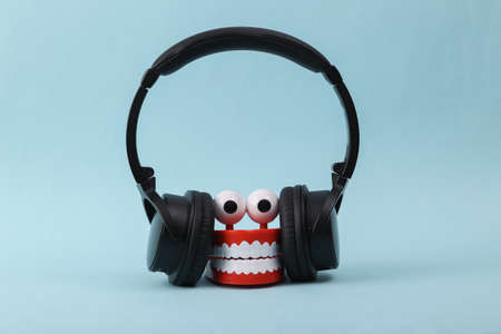 Funny toy clockwork jumping teeth with eyes listen music in stereo headphones on blue background.の写真素材