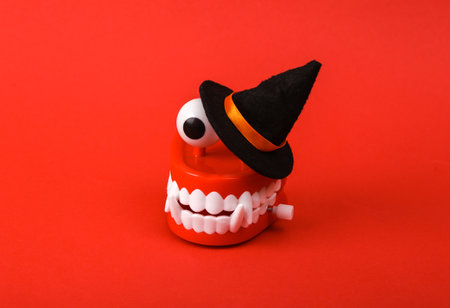 Funny toy clockwork jumping teeth monster with eyes and witch hat on red background. Halloween still...