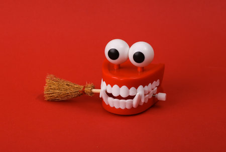 Halloween still life. Monster clockwork jaw with witch broom on red background