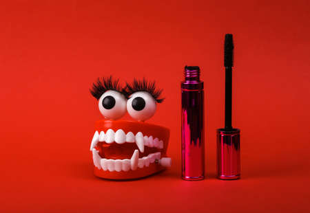 Funny toy clockwork jumping monster teeth with eyes and false eyelashes, mascara on red background....