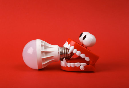 Funny toy clockwork jumping monster teeth with eyes and light bulb on red background.