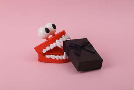 Funny toy clockwork jumping teeth monster with eyes and gift box on pink background.