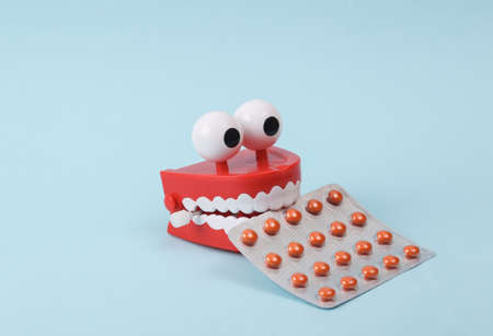 Funny toy clockwork jumping teeth with eyes and blister pills on blue background.