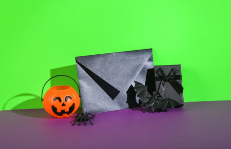 Halloween still life. Black envelope with a gift box and Halloween decor on a green-purple backgroundの写真素材