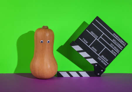Halloween pumpkin with eyes and movie clapperboard on a green-purple background. minimal layoutの写真素材