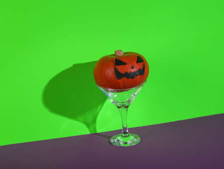 Halloween party. Halloween pumpkin with cocktail martini glass on green purple background. minimal layoutの写真素材