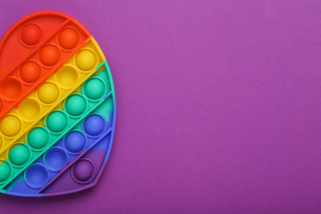 Pop it sensory rainbow antistress heart shaped toy on purple background. top view. copy spaceの写真素材