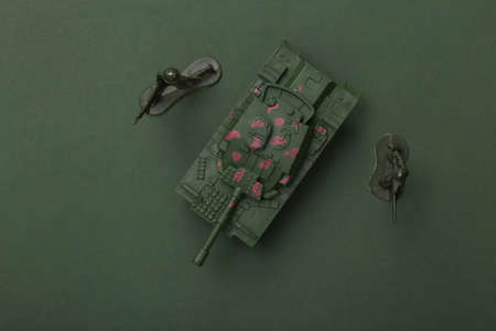 Toy plastic tank with soldiers on green background. top view