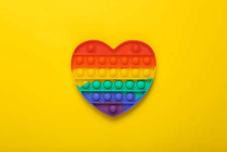 Pop it sensory rainbow antistress heart shaped toy on yellow background