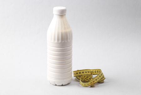 Plastic bottle of yoghurt and li milk with a measuring tape on a gray background. Diet, weight lossの写真素材