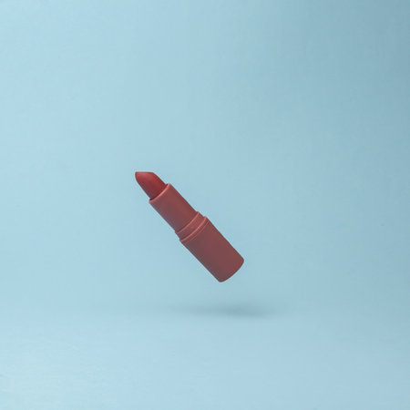 Red lipstick tube flying in antigravity on blue background with shadow. Levitation object in the air. Beauty and fashion concept. Creative minimal layoutの写真素材