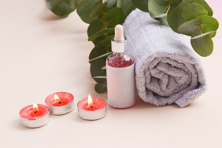 Spa salon, beauty concert. Serum bottle with towel and sprig of eucalyptus and candle on beige backgroundの写真素材