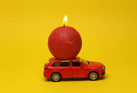 Model car with a flaming candle on a yellow backgroundの写真素材