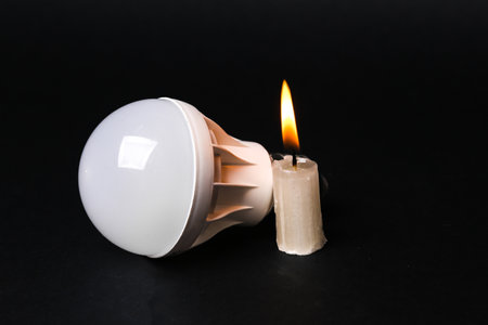 Modern led light bulb with burning candle on a black background. Progress.の写真素材