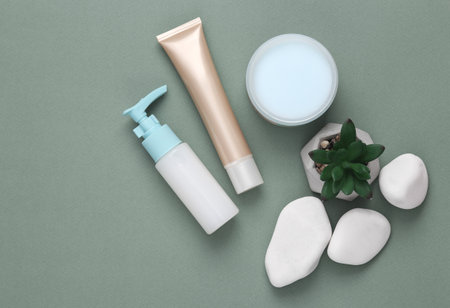 Beauty minimal still life. Bottle and jar of cream, tube of foundation and pebbles on green backgroundの写真素材