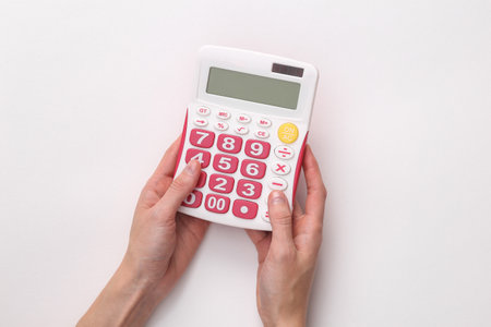 Female hands hold a white calculator with pink buttons on a gray backgroundの写真素材