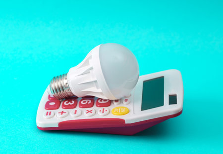 Electricity costs, save money concept, energy efficient and energy consumption of modern light bulbs. Calculator with light bulb on blue backgroundの写真素材
