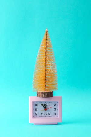 Clock with a miniature Christmas tree on a turquoise background. Merry christmas, new year concept