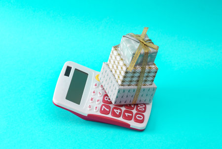 Stack of Christmas gift boxes wrapped in bow with calculator on a turquoise background