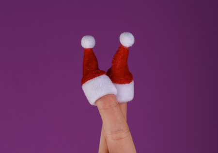 Mini Santa hats on the fingers of female hand on purple background. christmas conceptの写真素材