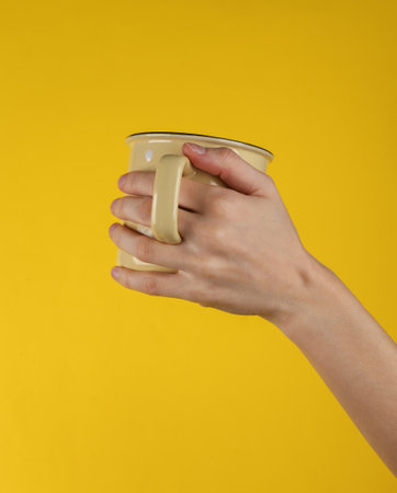 Ceramic yellow cup in female hand on yellow background
