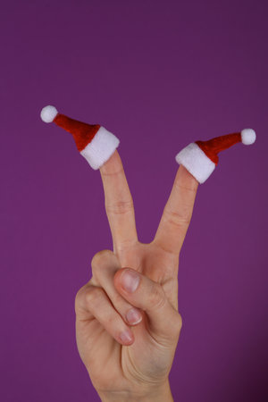 Mini Santa hats on the fingers of female hand on purple background. christmas conceptの写真素材