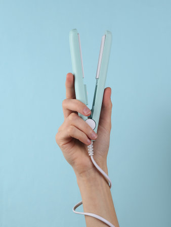 Mini Hair straightener in female hand on a blue background.の写真素材