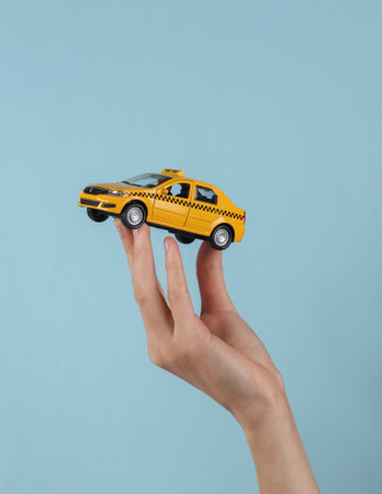 Mini model yellow taxi car in female hand on a blue background.の写真素材