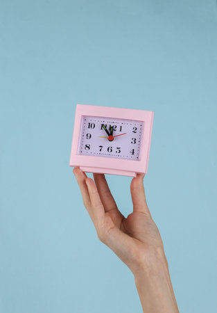 Square table clock in female hand on blue background.の写真素材