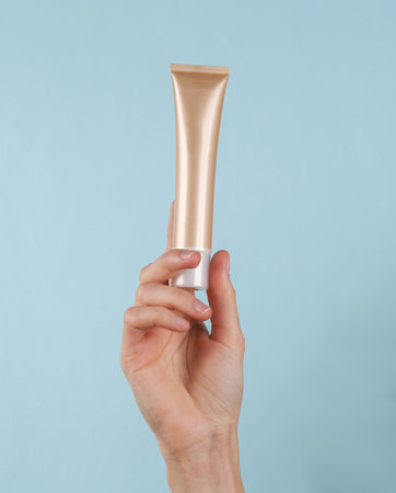 Foundation cream tube in female hand on blue backgroundの写真素材