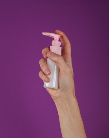 Cream bottle in female hand on purple background.