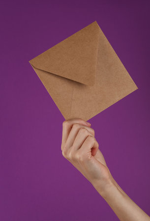 Craft envelope in female hand on a purple background.
