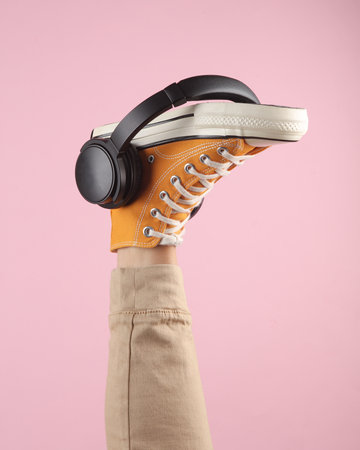 Female leg in stylish retro 80s yellow sneakers with headphones on a pink background. creative ideas