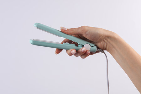 Woman's hand holding a hair straightener on a white backgroundの写真素材