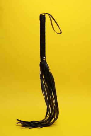Leather sex whip levitating on yellow background. dominance. sex games.の写真素材