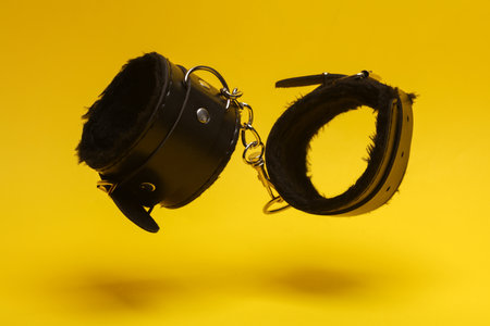 Leather bdsm handcuffs levitating on yellow background. dominance. sex games.