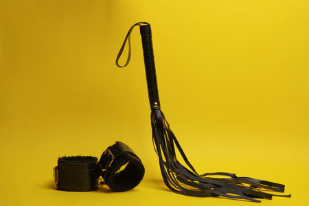Leather bdsm handcuffs and whip levitating on yellow background. dominance. sex games.