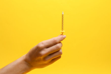 Hand holding birthday candle on yellow backgroundの写真素材