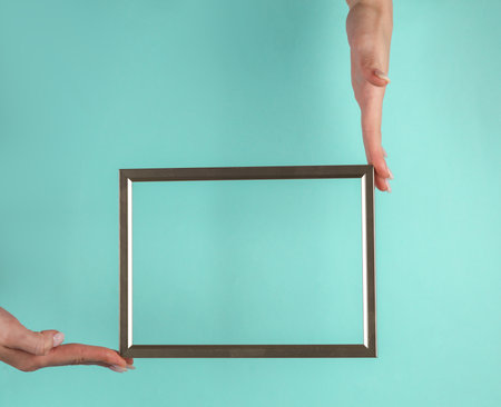 Woman's hands holding a golden blank frame on a blue backgroundの写真素材