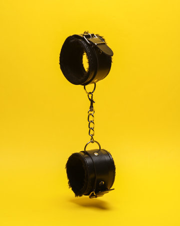 Leather bdsm handcuffs levitating on yellow background. dominance. sex games.