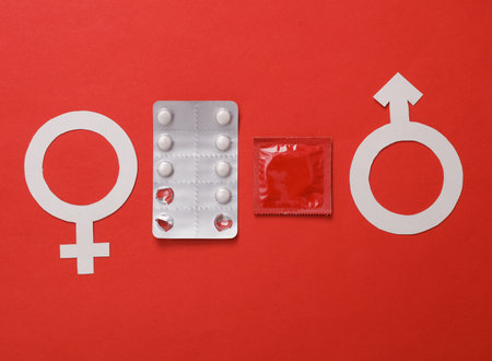 Contraceptive pills with condom and male and female gender symbol on red background. Birth Controlの写真素材
