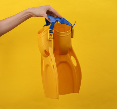 Woman's hand holding yellow diving fins on yellow background