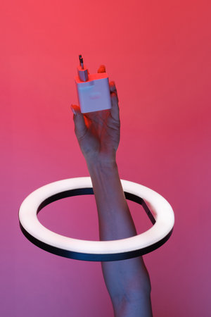 Woman's hand holds charger adapter through led ring lamp in red blue neon gradient light. creative...