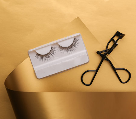 False eyelashes with lash curler on a luxurious golden backgroundの写真素材