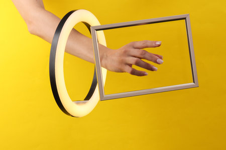 Woman's hand through led ring lamp and frame on yellow background. creative ideas.