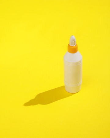 Bottle of glue on a yellow background with a long shadow. minimalist photoの写真素材